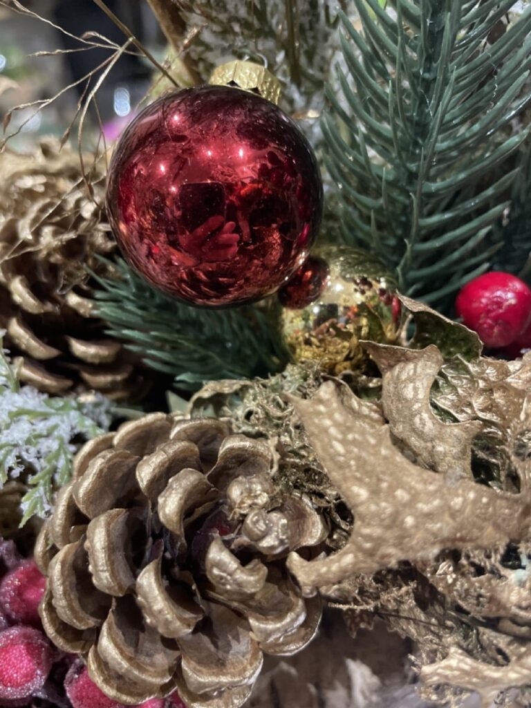 Joli plan sur une décoration de Noël composée d’une boule rouge brillante, de pommes de pin dorées et de branches de sapin.