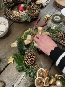 Création d’une couronne de Noël florale lors d’un atelier, avec branches de sapin, pommes de pin, oranges séchées et ruban doré