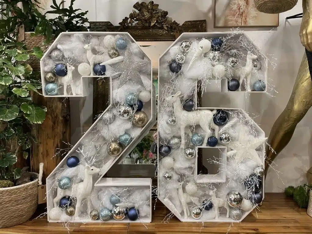 Grande composition décorative représentant le chiffre 26, ornée de fleurs, feuillages et éléments hivernaux blancs et bleus, évoquant la tendresse, le ciel bleu et les vœux poétiques 2026 du fleuriste Yann-h2o.