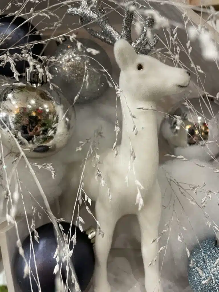Détail d’une décoration hivernale avec un animal décoratif blanc entouré de branches légères et de boules argentées et bleues, évoquant la tendresse, le calme et la poésie des vœux 2026 du fleuriste Yann-h2o.