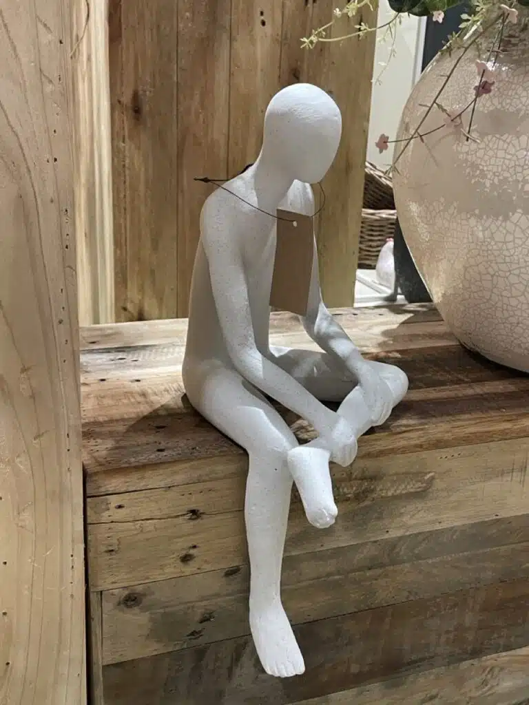Sculpture décorative minimaliste représentant une figure assise en matière texturée claire, mise en scène sur du bois brut, tendance design repérée à Maison&Objet.