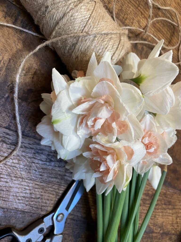 Bouquet de narcisses blanc et cœur pêche posé sur table en bois avec ficelle et sécateur – création artisanale fleuriste Yann-H2o Paris 11
