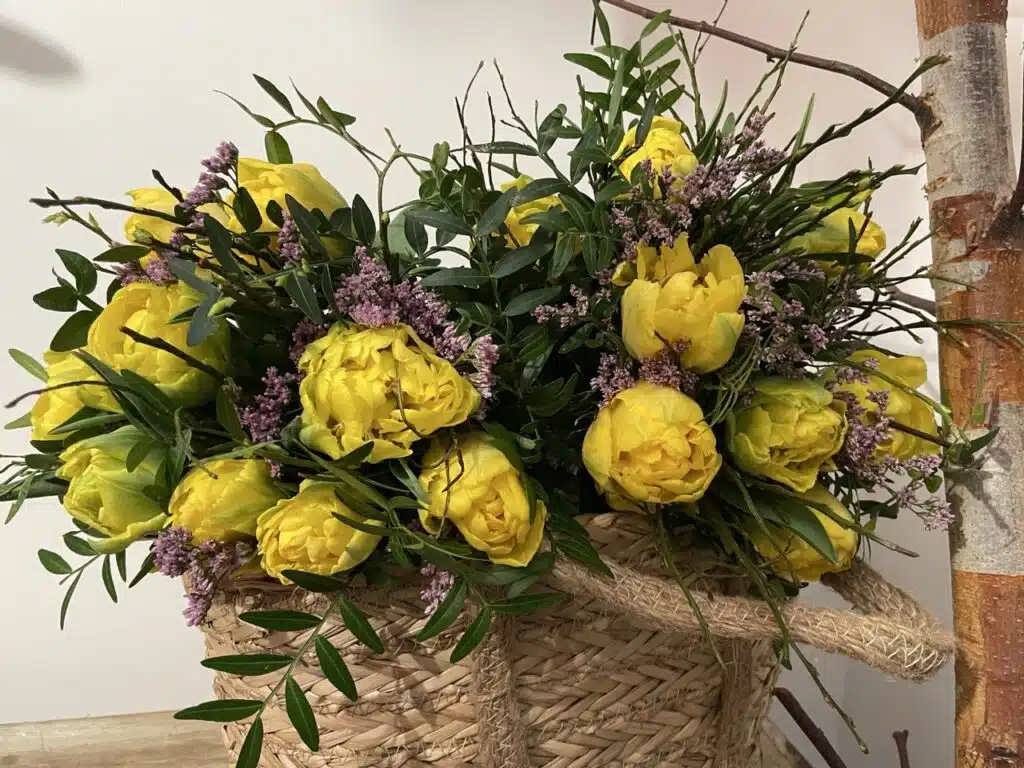 Bouquet de tulipes jaunes doubles dans un panier naturel, composé avec feuillage et fleurs de saison par le fleuriste Yann H2o à Paris.