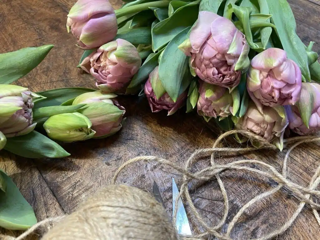 Tulipes doubles roses posées sur une table en bois avec ficelle naturelle dans l’atelier du fleuriste Yann H2o à Paris.