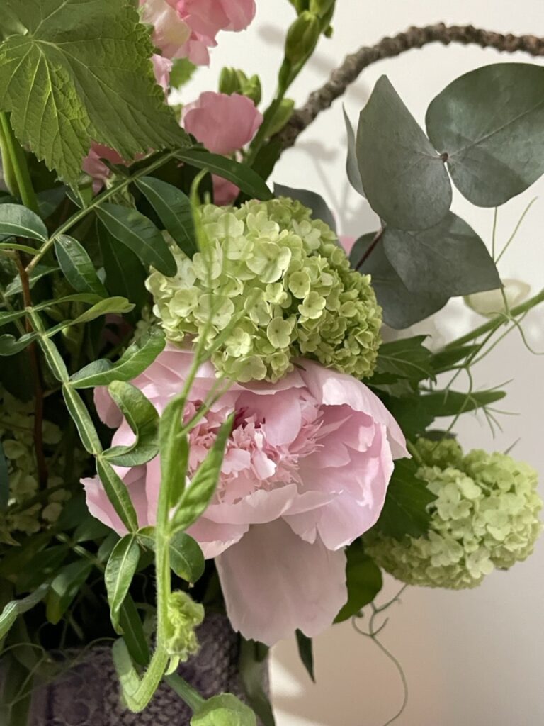 Détail d’une composition florale réalisée par Yann artisan fleuriste créatif à Paris 11 proche rue Roquette avec pivoines françaises roses, viburnum vert et feuillage de saison en livraison dans tout Paris