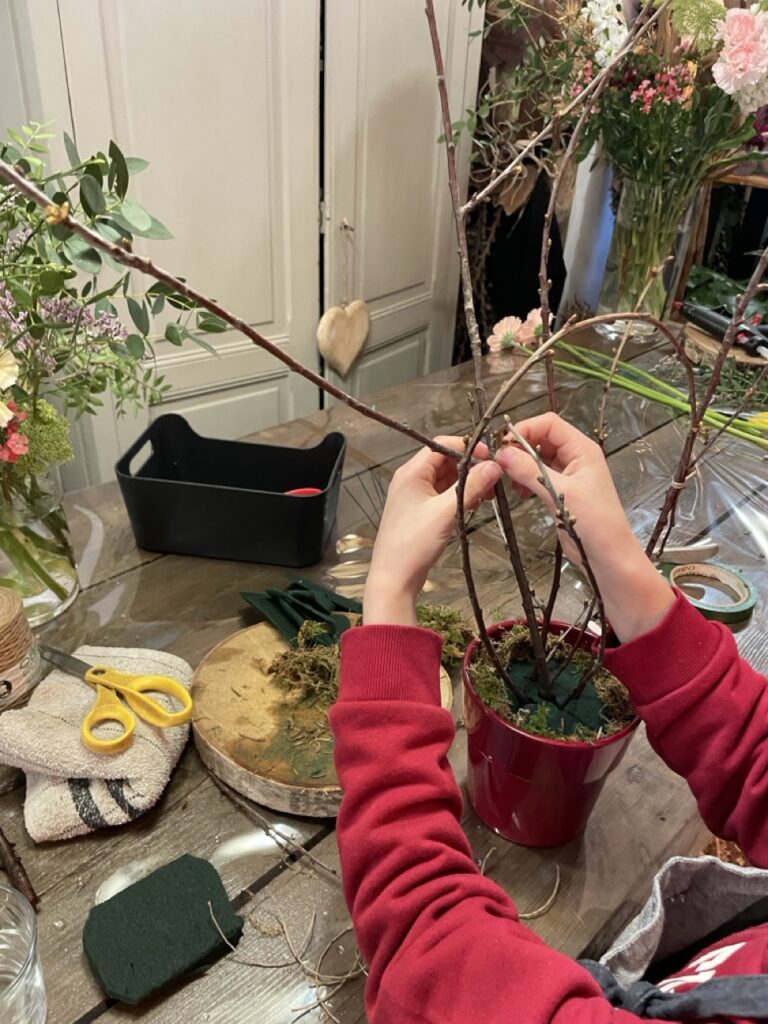Participant réalisant une structure végétale en branchages et fleurs de saison pendant un atelier de création végétale animé par Yann-H2o, artisan fleuriste à Paris 11.
