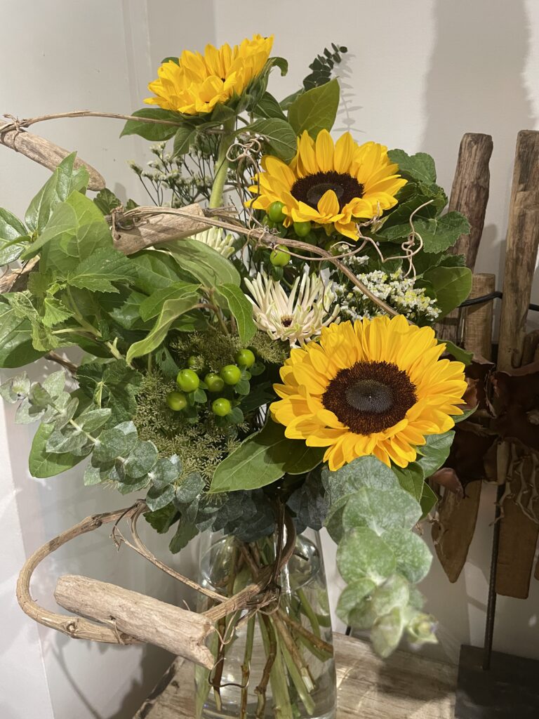 Bouquet de tournesols de saison aux feuillages naturels, composé par un artisan fleuriste à Paris 11. Création florale disponible en livraison de fleurs dans tout Paris.