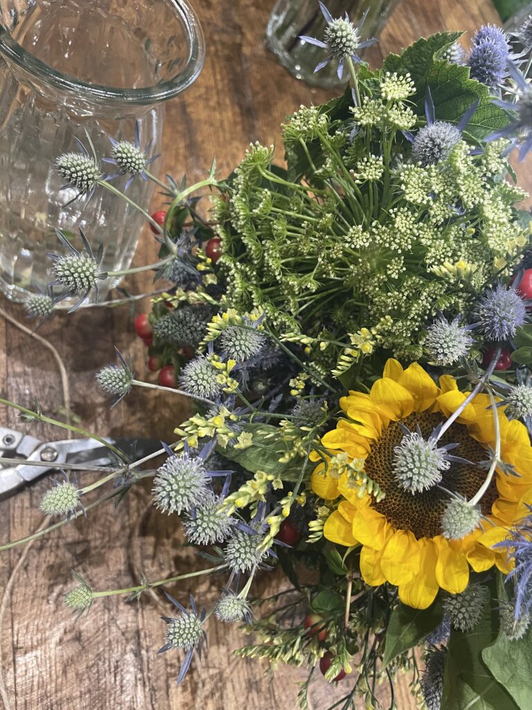 Bouquet de saison composé d'un tournesol, de chardons bleus, de fleurs champêtres et de baies décoratives, créé par un artisan fleuriste Yann-H2o à Paris 11 et disponible en livraison dans tout Paris.