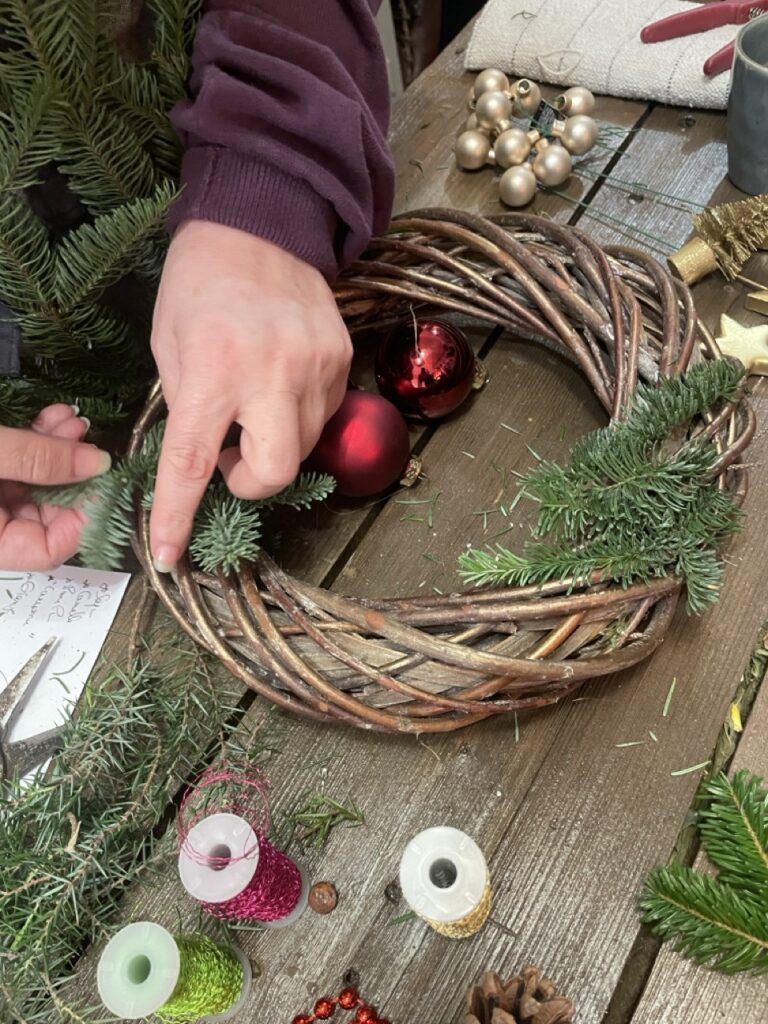 Réalisation d'une couronne végétale de Noël lors d'un atelier créatif animé par Yann-H2o, artisan fleuriste à Paris 11. Les participants assemblent branchages, sapin et décorations naturelles pour créer une composition de saison.