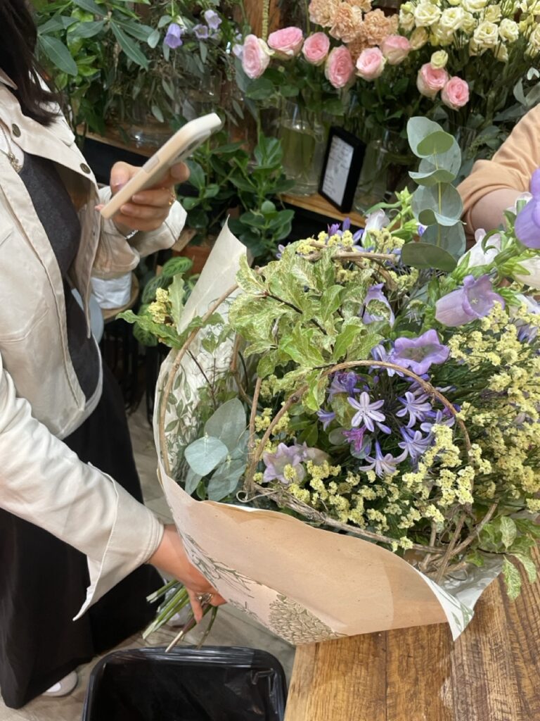 Une participante présente sa création florale réalisée pendant un atelier chez Yann-H2o, artisan fleuriste à Paris 11. Une composition de fleurs de saison mêlant végétaux, branchages et fleurs fraîches.