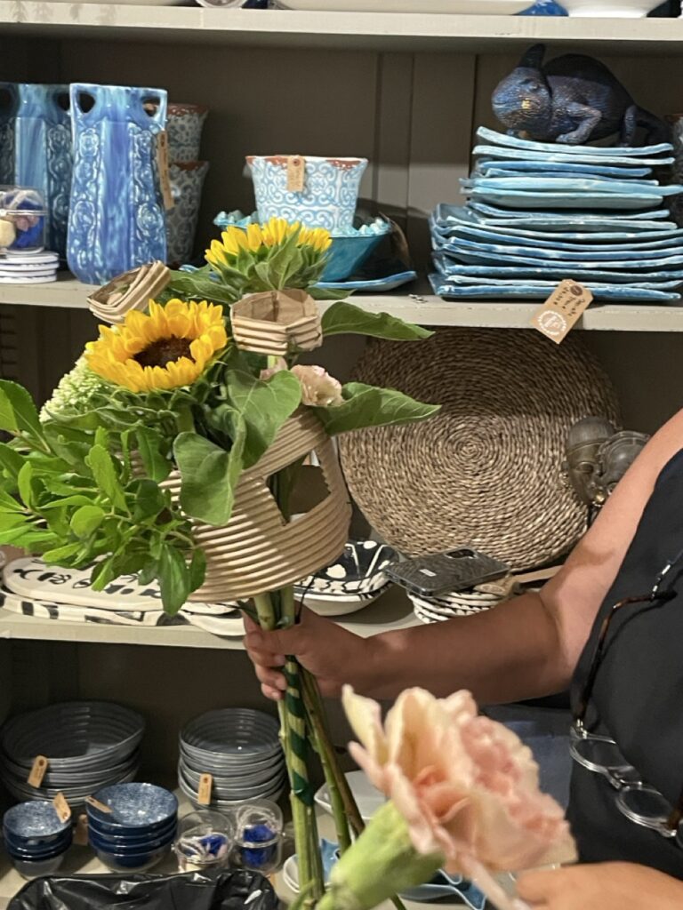Participant présentant une création florale contemporaine réalisée avec des fleurs de saison et une structure en carton lors d'un atelier convivial animé par Yann-H2o, artisan fleuriste créateur à Paris 11. Chaque atelier est une invitation à créer librement, dans la bonne humeur, avec des matières originales et des végétaux de saison.
