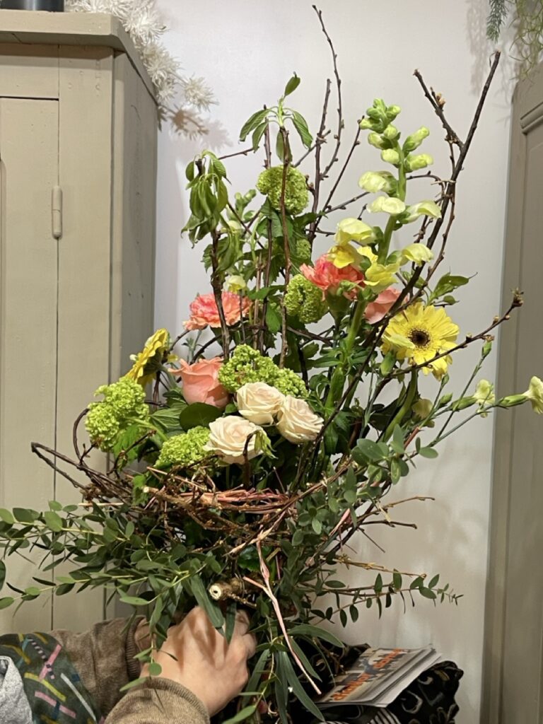 Participant présentant une création florale contemporaine réalisée avec des fleurs de saison, des branchages et un nid végétal lors d'un atelier convivial animé par Yann-H2o, artisan fleuriste créateur à Paris 11. Chaque création exprime la créativité de son auteur dans une ambiance chaleureuse et bienveillante.