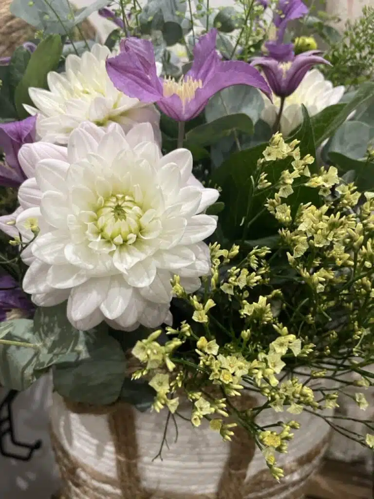 Création florale associant des dahlias blancs, des clématites violettes, du limonium, de l'eucalyptus et des feuillages de saison, réalisée par Yann-H2o, artisan fleuriste à Paris 11.