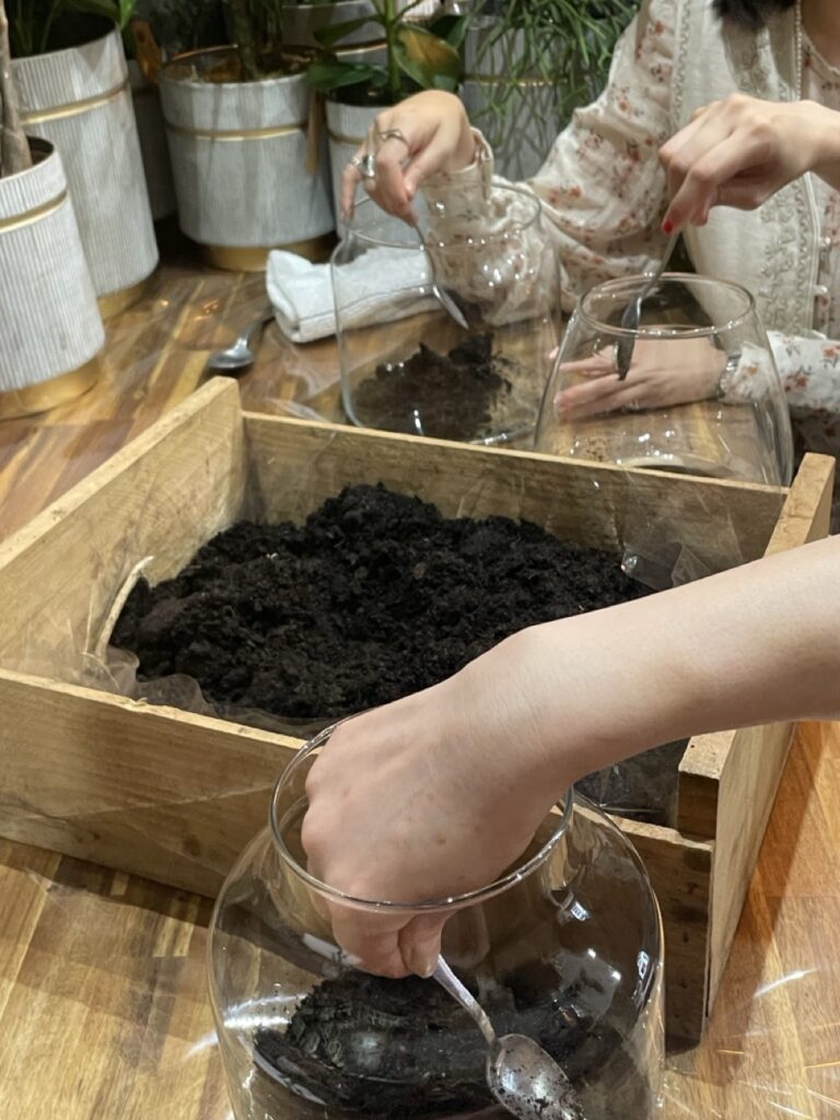 Participants réalisant un terrarium végétal pendant un atelier floral animé par Yann-H2o, artisan fleuriste à Paris 11. Découverte des techniques de composition avec des végétaux et des fleurs de saison.
