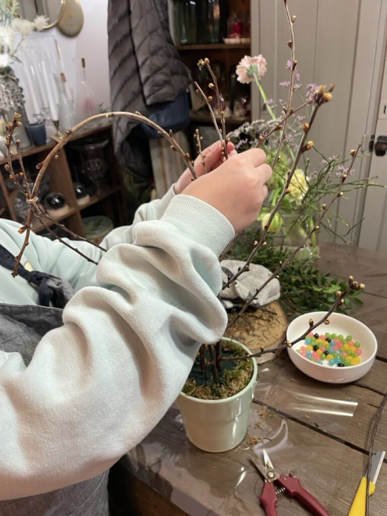 Participant réalisant une création végétale avec des branchages et des fleurs de saison lors d'un atelier créatif animé par Yann-H2o, artisan fleuriste à Paris 11.