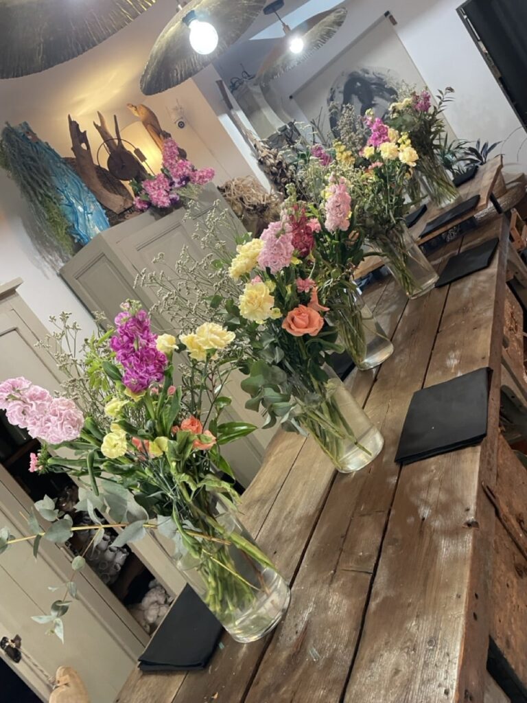 Bouquets de fleurs roses, jaunes et orangées disposés sur une grande table en bois lors d’un atelier floral privatisé chez Yann-H2o, artisan fleuriste à Paris 11.