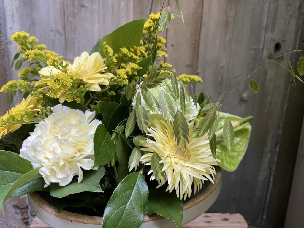 Gros plan sur un bouquet de fleurs aux gerberas jaune pâle, œillets blancs, anthurium vert et graminées aériennes, création de Yann-H2o à Paris 11.