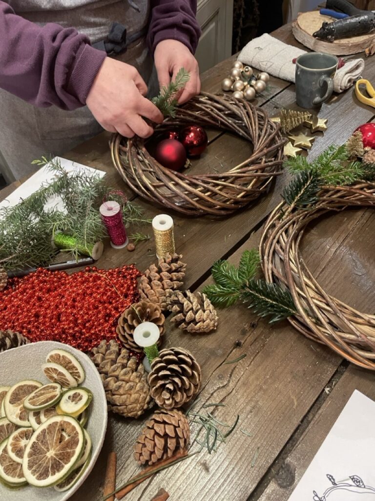 Création d’une couronne de Noël lors d’un atelier floral à Paris 11 chez Yann-H2o, avec branches de sapin, pommes de pin et décorations festives.